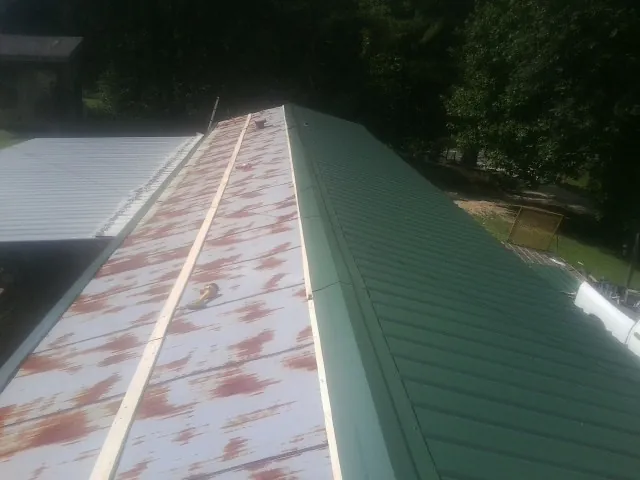 Old rusted panels beside newly installed green metal roofing — Wind Damage Roof Repair by Roofing Brothers in Jennings