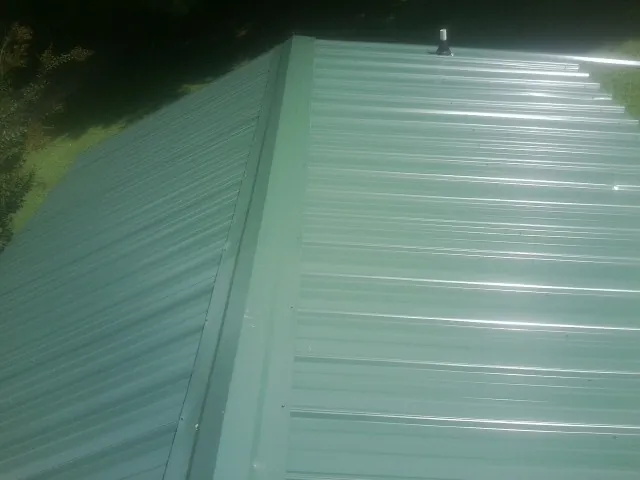 New green metal panels meeting at the ridge of a roof — Flat Roof Repair work by our crew in Jennings