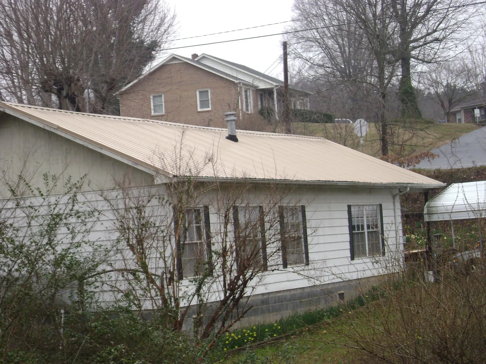 Tan metal roof on a white sided house set into a hillside — Commercial Roofing by Roofing Brothers in Jennings